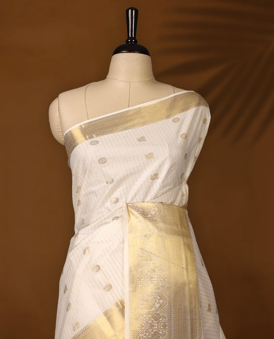 Elegant off white colour cotton Kerala saree with golden buttas, rich zari border, and intricately woven pallu featuring floral and temple motifs. Perfect for festive occasions, paired with a matching blouse.