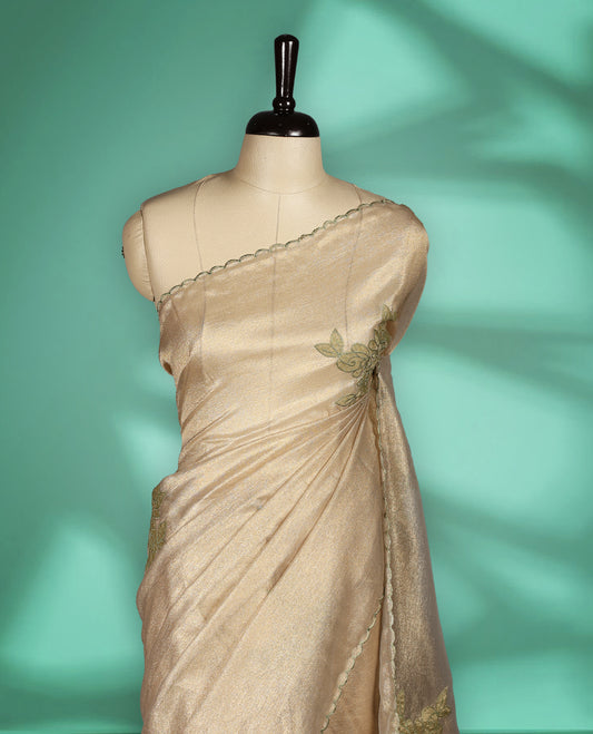Beige gold colour organza designer saree featuring a subtle shimmer woven body with delicate green floral thread embroidery, scalloped thread detailing along the border and pallu paired with matching blouse.