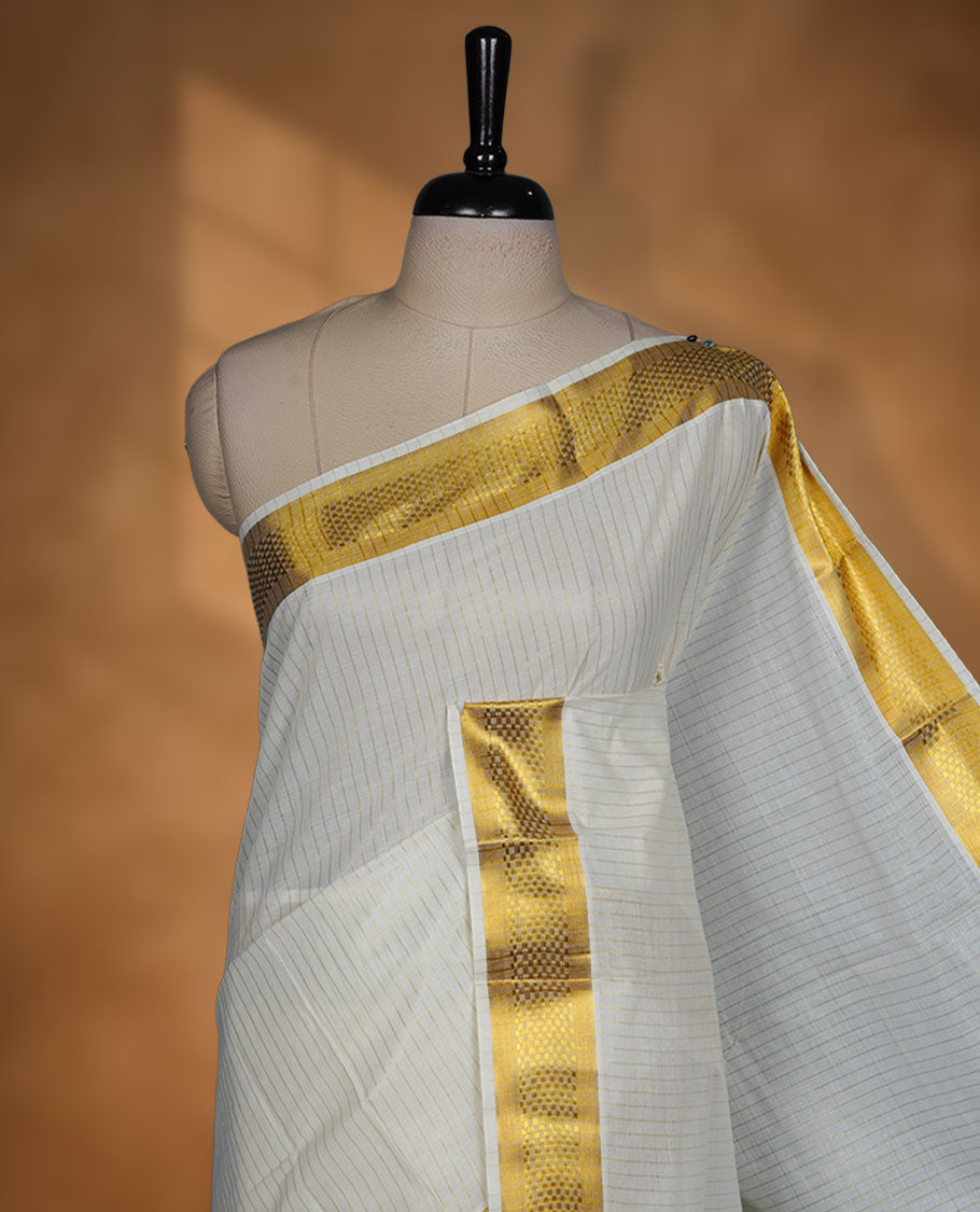 Off-white colour Kerala cotton saree with fine striped texture, rich golden zari border, and traditional motif pallu, paired with a matching blouse.