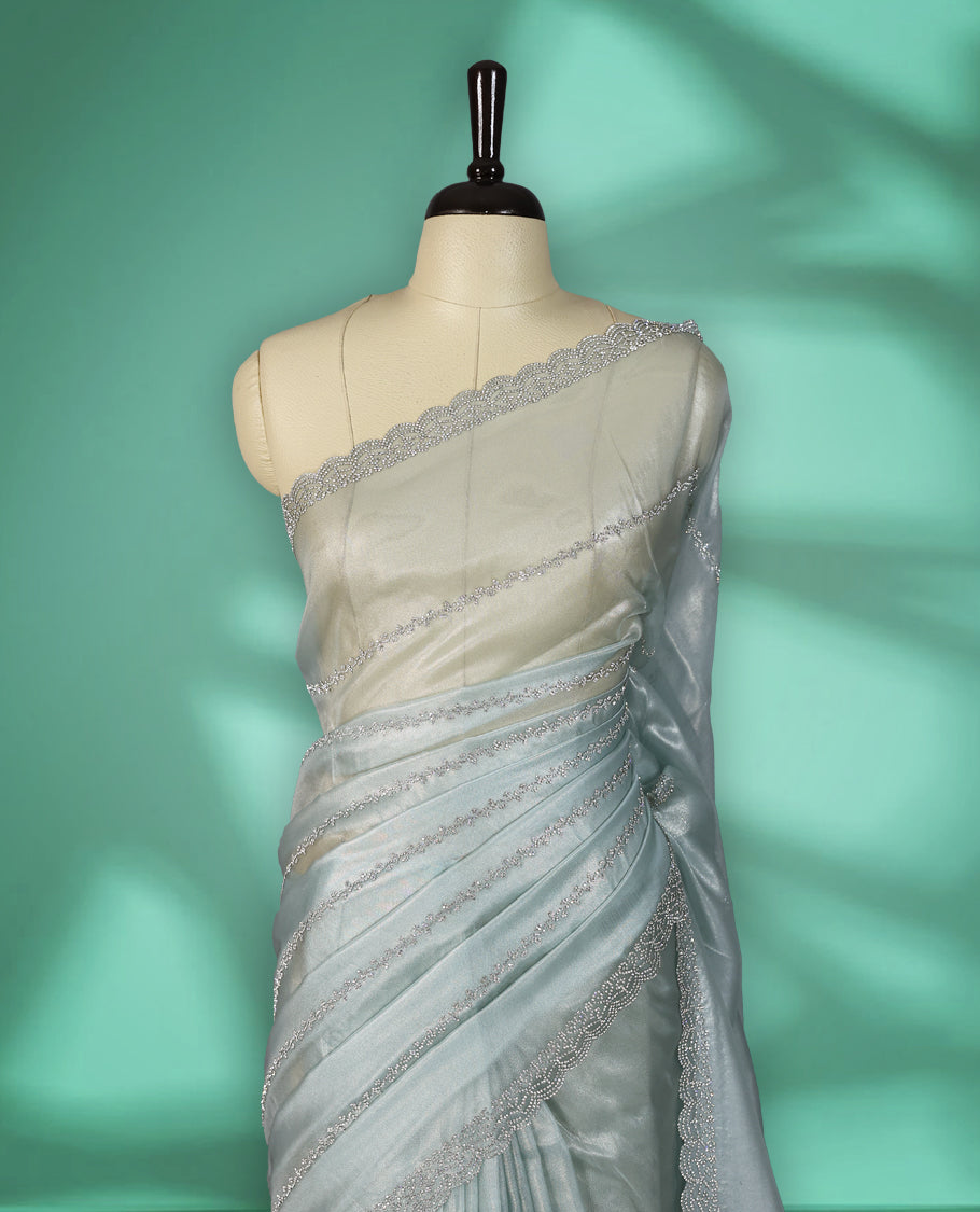 Icy blue colour net shimmer fancy saree adorned with subtle horizontal White stone patterns on the body, paired with a delicate stone worked border, with matching blouse
