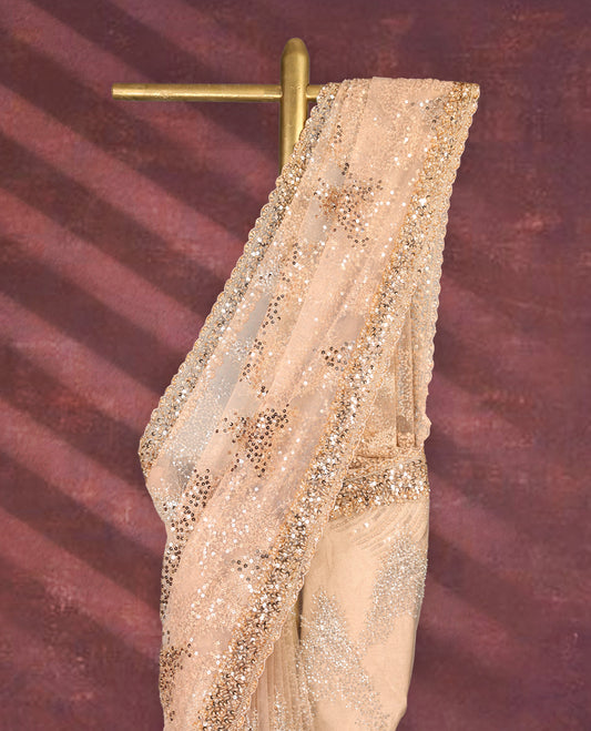 Pastel peach colour net designer saree embellished with all over shimmering sequin work in diagonal patterns and a heavily sequined border, exuding glamour and elegance, paired with a matching worked blouse for a striking look