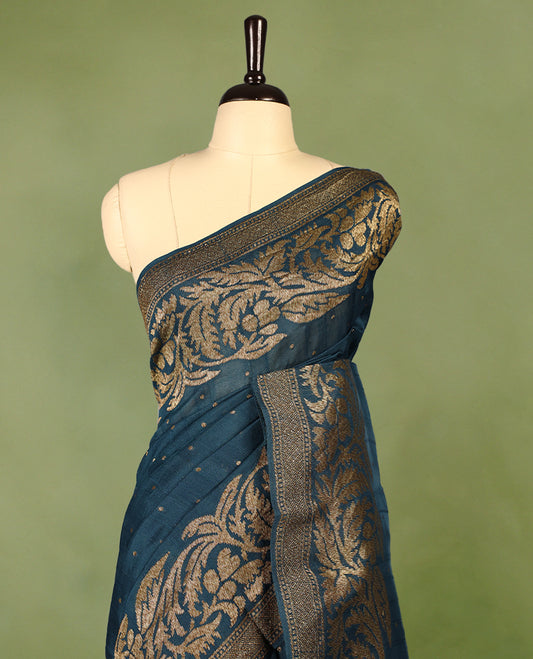 Deep teal colour Tussar Banaras saree adorned with delicate golden zari motifs on the body, rich floral woven zari border and grand pallu, paired with a matching blouse for an elegant and regal traditional look.