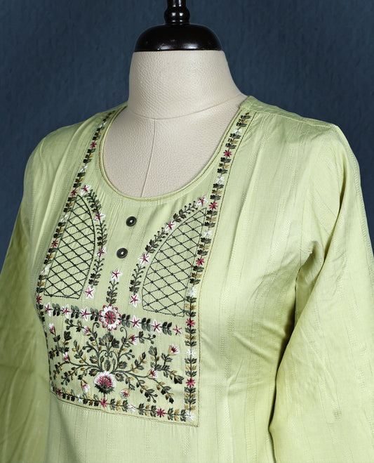 Light green colour kurti with subtle vertical self stripes, highlighted by an intricately embroidered yoke in floral and geometric patterns, featuring a round neckline with button accents and three quarter sleeves.