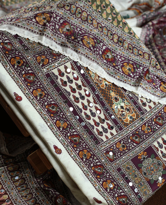 Off white colour churidhar material beautifully detailed with grape colour traditional paisley and floral prints, mirror work highlights, paired with a plain white bottom and a matching printed dupatta with lace border.
