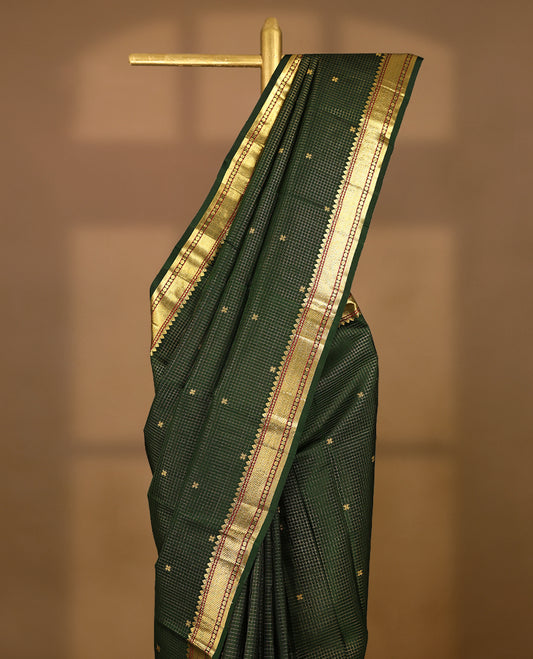 Dark green Colour traditional Kancheepuram silk saree adorned with an antique zari grid pattern and small golden Floral motifs on the body, featuring a border with paisley and Rudraksham motifs, and paired with a matching blouse.