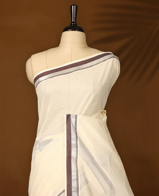 Classic off white colour cotton Kerala saree with elegant coffee brown and silver zari borders, exuding timeless charm. Paired with a matching blouse, perfect for traditional functions and cultural festivities.