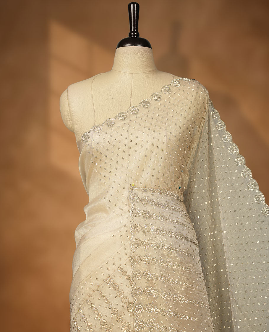 Beige colour net shimmer fancy saree adorned with gold stone buttas all over the body, paired with a delicate stone worked border, with matching blouse