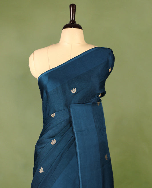Deep teal colour crepe Banaras saree featuring small zari Floral Motifs across the body, without border, a sleek texture, and a rich golden zari pallu with geometric patterns, paired with a matching blouse for a graceful festive look