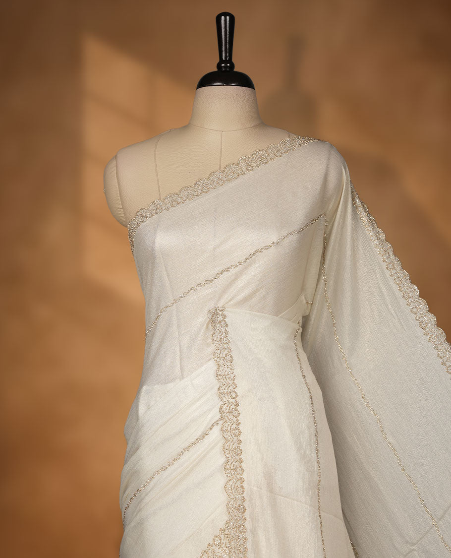 Pastel Cream Colour shimmer fancy saree adorned with scattered gold stone buttas all over the body, paired with a delicate stone worked border and matching blouse