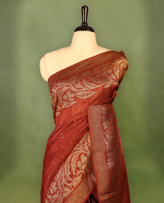 Rust Orange colour Tussar Banaras saree adorned with delicate golden zari motifs on the body, rich floral woven zari border and grand pallu, paired with a matching blouse for an elegant and regal traditional look.
