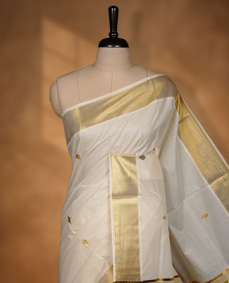 Off-White colour cotton Kerala saree adorned with subtle gold zari buttas, a broad kasavu border, and a richly woven traditional pallu, paired with a matching blouse.