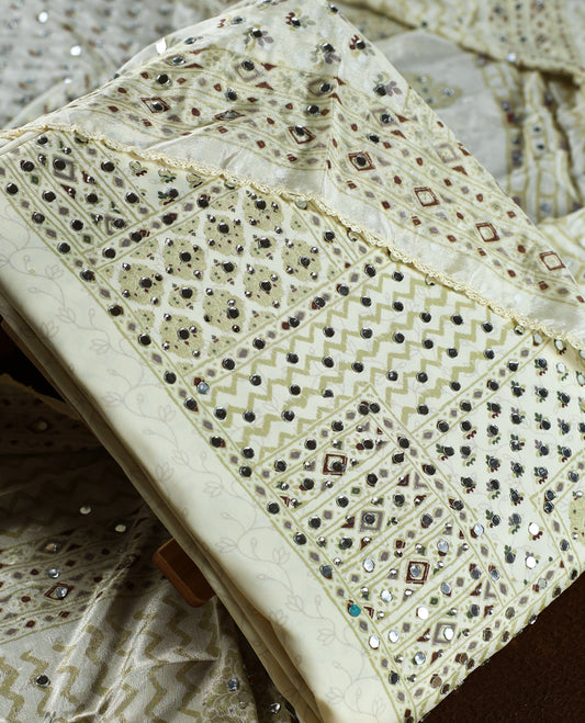 Cream colour churidar material adorned with intricate geometric designs and sparkling mirror work, paired with a plain matching bottom and dupatta.