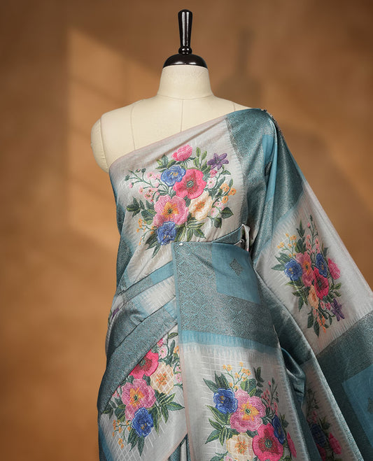 Blue color semi tussar Banarasi saree featuring vibrant multi-color floral prints across the body, with geometric zari patterns, and a matching blouse detailed with silver woven buttas.