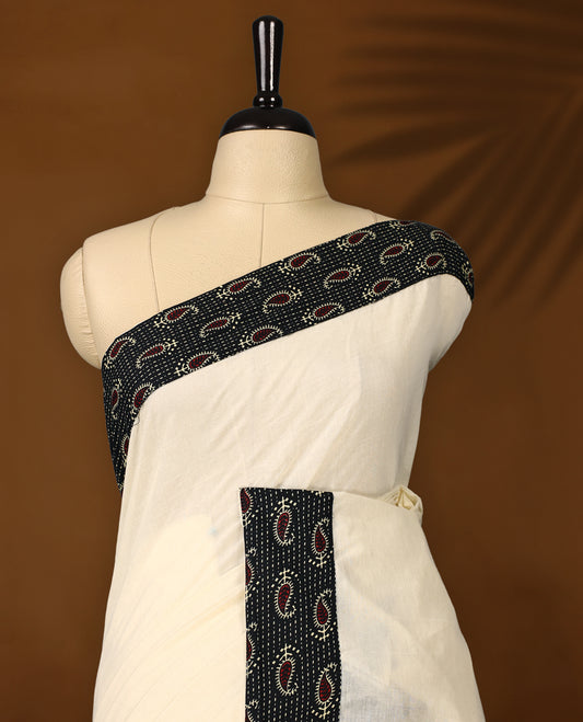 Off white colour cotton Kerala saree accentuated with a black printed border featuring red paisley motifs and delicate white dotted patterns, paired with a matching printed blouse for a classic ethnic charm