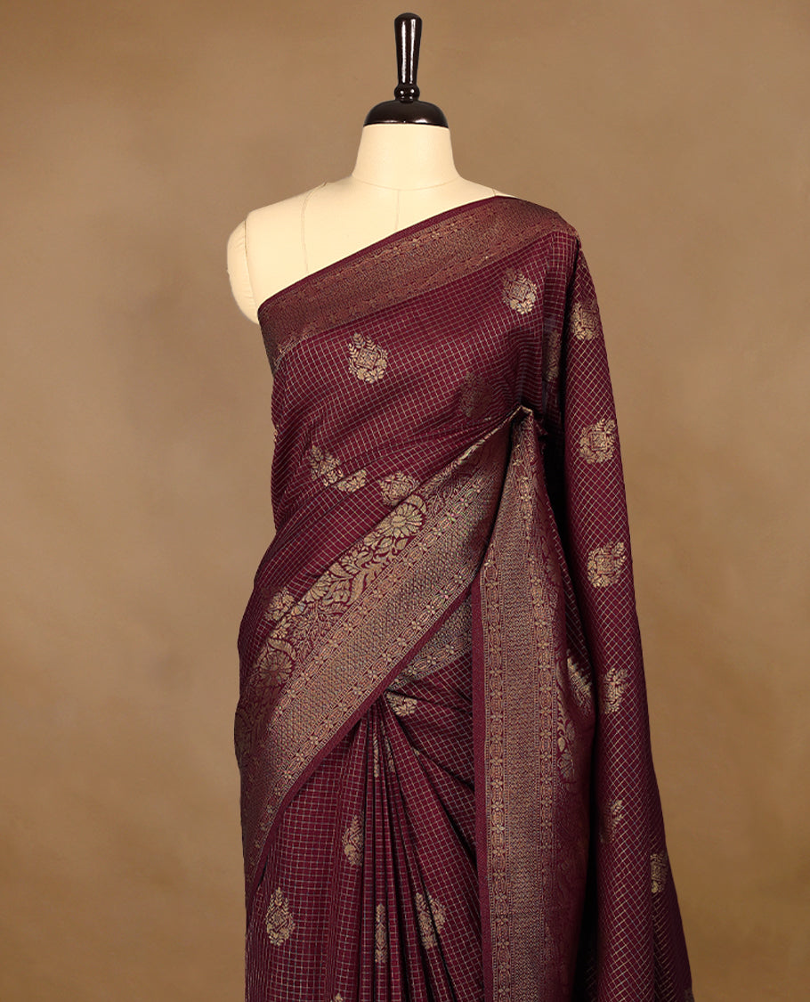 Maroon coloured semi Banaras georgette saree featuring golden Zari checks with floral motifs on the body, complemented by a self coloured traditional border with floral kodi design and a matching blouse.
