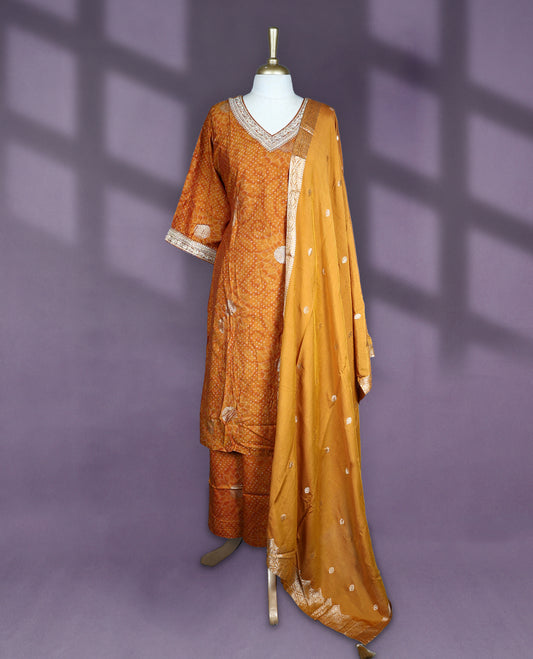 Deep Mustard colour salwar set with V neck and elbow sleeves featuring bandhani inspired dotted pattern with gold motifs paired with matching bottom and dupatta with tassel detail