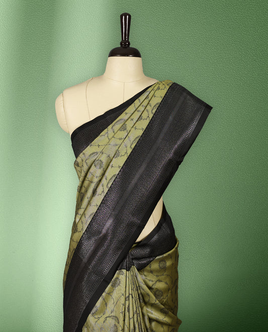 Pastel mustard green colour semi silk saree featuring neem zari floral kodi motifs all over the body, complemented by a pure black woven border with geometric detailing, with matching blouse.