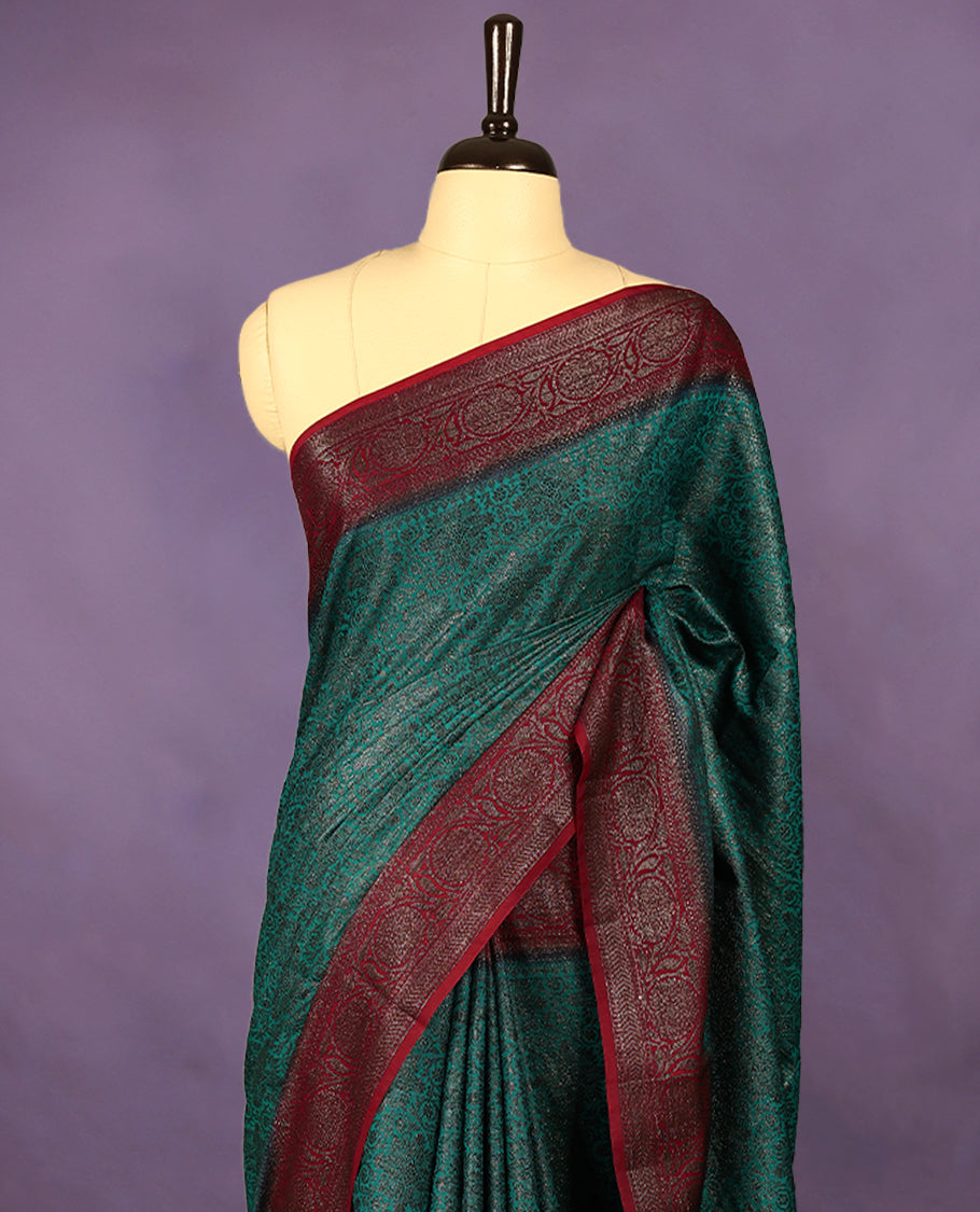 Dark aqua green colour semi Banaras Katan saree featuring an antique zari jacquard body, complemented by a contrasting traditional border with a floral kodi design, paired with a matching blouse.