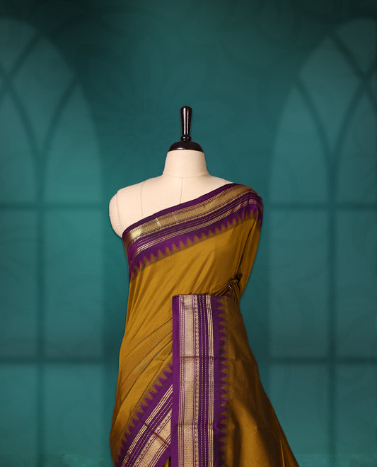 Mustard yellow semi silk saree with plain body, royal ourole pallu and matching purple border adorned with golden zari, accented with temple motifs along the edges, Paired with a matching blouse, perfect for festive occasions.