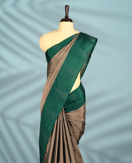 Taupe colour semi silk saree adorned with minimal geometric weave detailing, enhanced by a deep emerald green border, comes with a matching blouse.