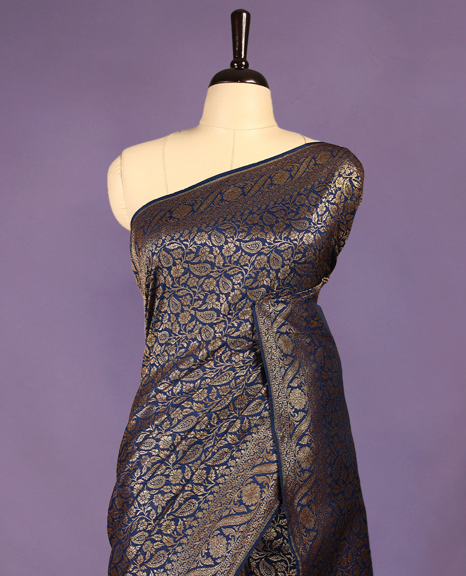 Navy blue colour semi Banaras Katan silk saree featuring intricate Antique Bronze zari floral and vine patterns woven throughout the body, enhanced with a rich traditional border and detailed pallu, paired with a matching blouse piece.