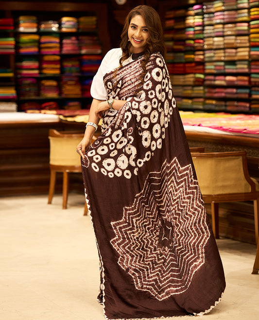 Medium coffee brown colour modal satin crepe saree featuring intricate hand done Shibori and Bandhej designs, enhanced by its smooth texture and paired with a matching blouse.