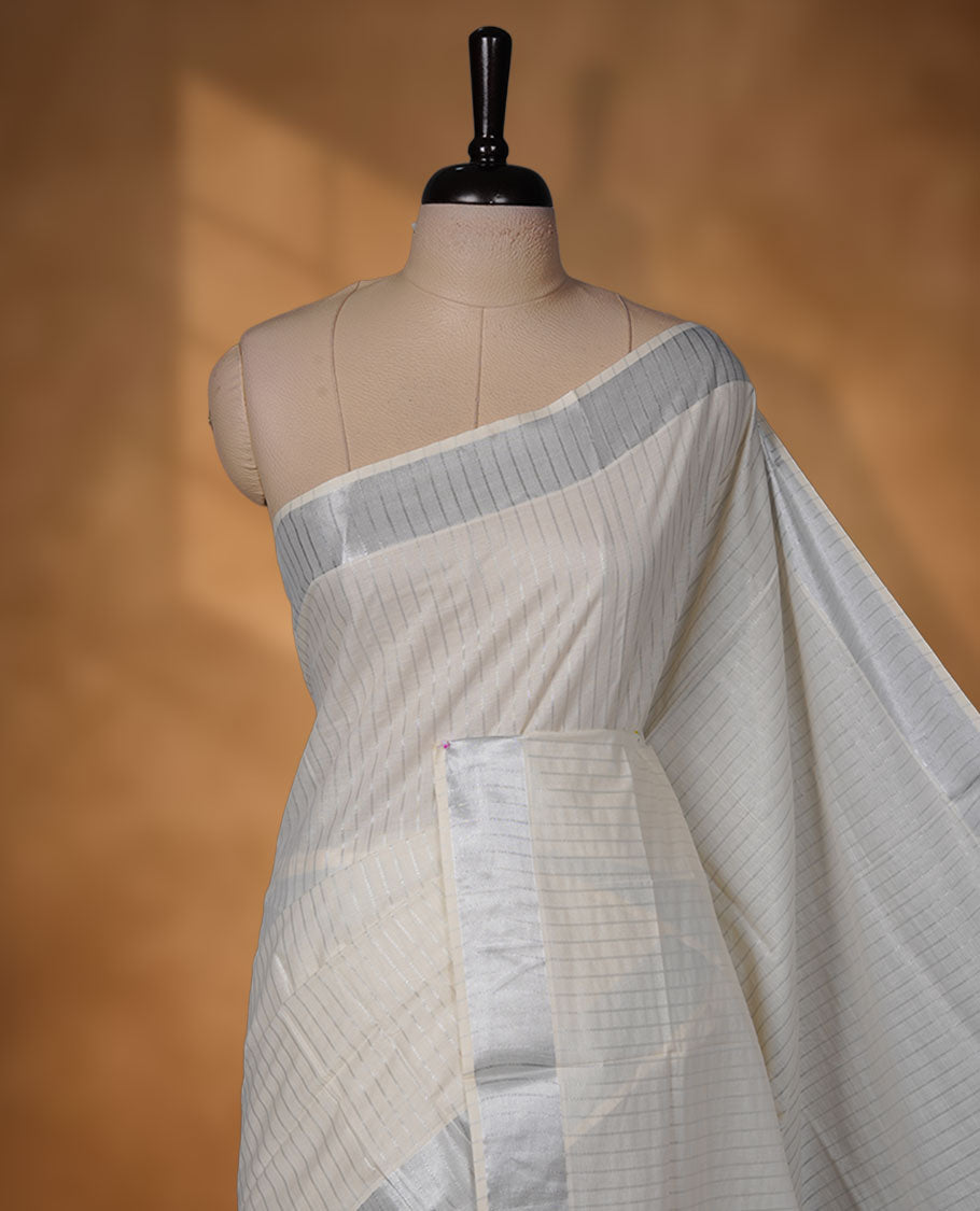 Off-white colour cotton Kerala saree featuring a silver line pattern, finished with an elegant silver kasavu border along the edges and pallu, and paired with a matching blouse.