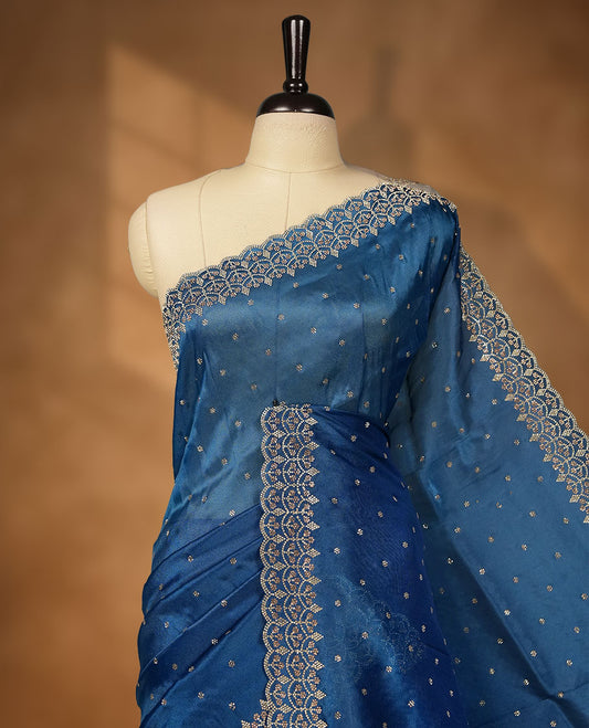 Blue colour net shimmer fancy saree adorned with white stone buttas all over the body, paired with a delicate stone worked border, with matching blouse