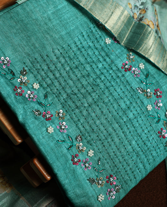 Light peacock green colour churidhar material adorned with floral embroidery and sewn glass beads on the yoke, paired with a plain green bottom and a beige dupatta featuring floral prints.