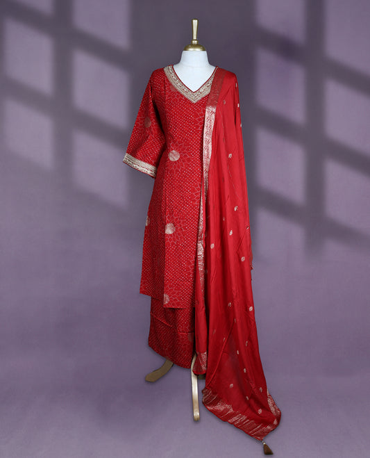 Deep red colour salwar set with V neck and elbow sleeves featuring bandhani inspired dotted pattern with gold motifs paired with matching bottom and dupatta with tassel detail