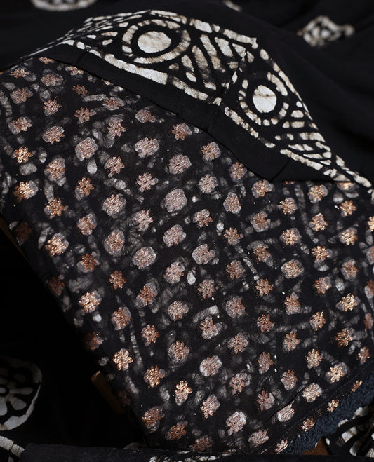 Black colour churidhar material adorned with gold and copper toned floral patterns and bold block designs, paired with a plain matching bottom and stylish dupatta, perfect for festive evenings and traditional gatherings.