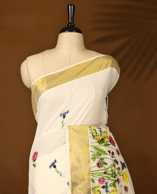 Elegant off white colour cotton Kerala saree with vibrant floral prints and a rich golden zari border, paired with a matching blouse. Perfect for festive occasions and day events with a graceful, natural charm.