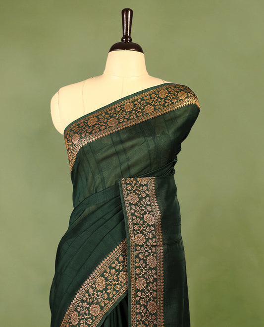 Bottle Green colour Tussar Banaras saree featuring a plain body, rich floral woven zari border and grand pallu, paired with a matching blouse for an elegant and regal traditional look.
