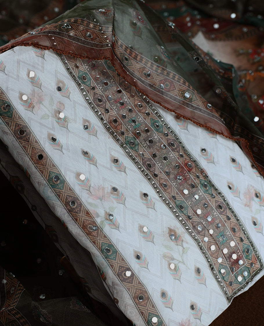 Elegant white churidhar material adorned with mirror work and subtle floral prints, enhanced by a rich green brown printed dupatta with sequin highlights, paired with a plain white bottom for a classy festive look.