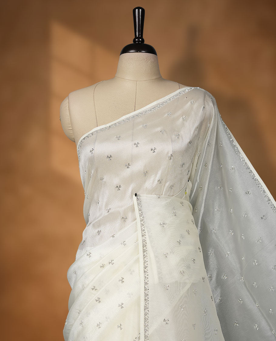 Off white Colour net shimmer fancy saree adorned with scattered white stone buttas all over the body, paired with a delicate stone worked border and matching blouse featuring floral vine stone embroidery