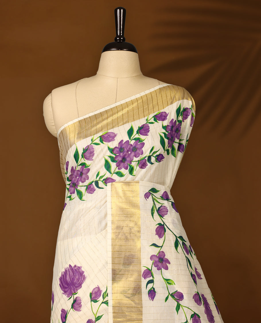 Elegant Off white colour cotton Kerala saree with hand-painted purple floral motifs, highlighted by a rich golden zari border and pallu paired with matching blouse.