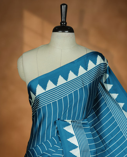 Teal Blue colour semi modal saree featuring bold white geometric borders and fine stripe detailing, finished with an oversized white circular motif on the pallu, paired with a matching printed blouse.