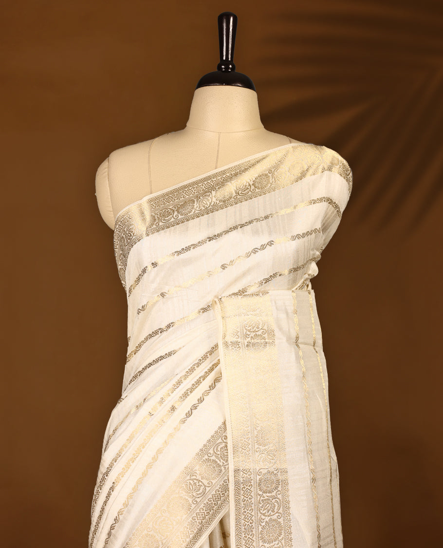 Elegant Off White colour Tussar Kerala saree featuring a Floral Kodi Stripes across body, muted gold zari banarasi Style border, and a striking Gold Zari woven Bold pallu, paired with a matching blouse.