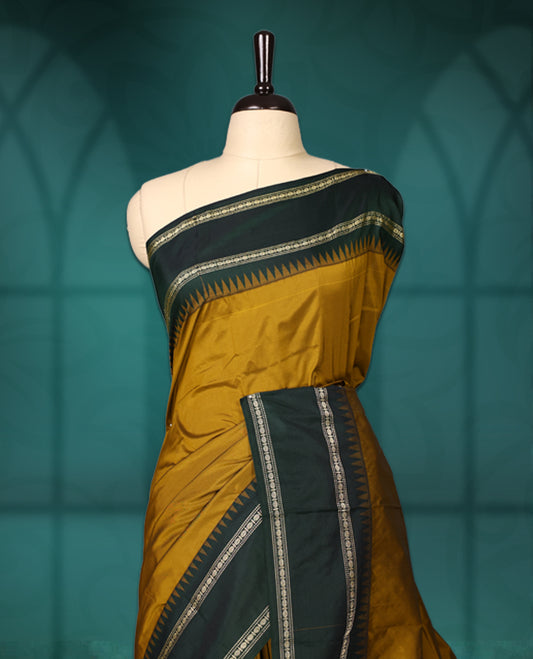 Mustard semi silk saree with plain body, vibrant deep green pallu and matching green border adorned with golden zari, accented with temple motifs along the edges, Paired with a matching blouse, perfect for festive occasions.