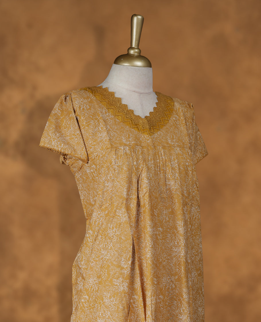 Mustard colour NStyle nighty featuring white floral patterns,a V neckline and thread lace border, short sleeves, and a full ankle-length design.
