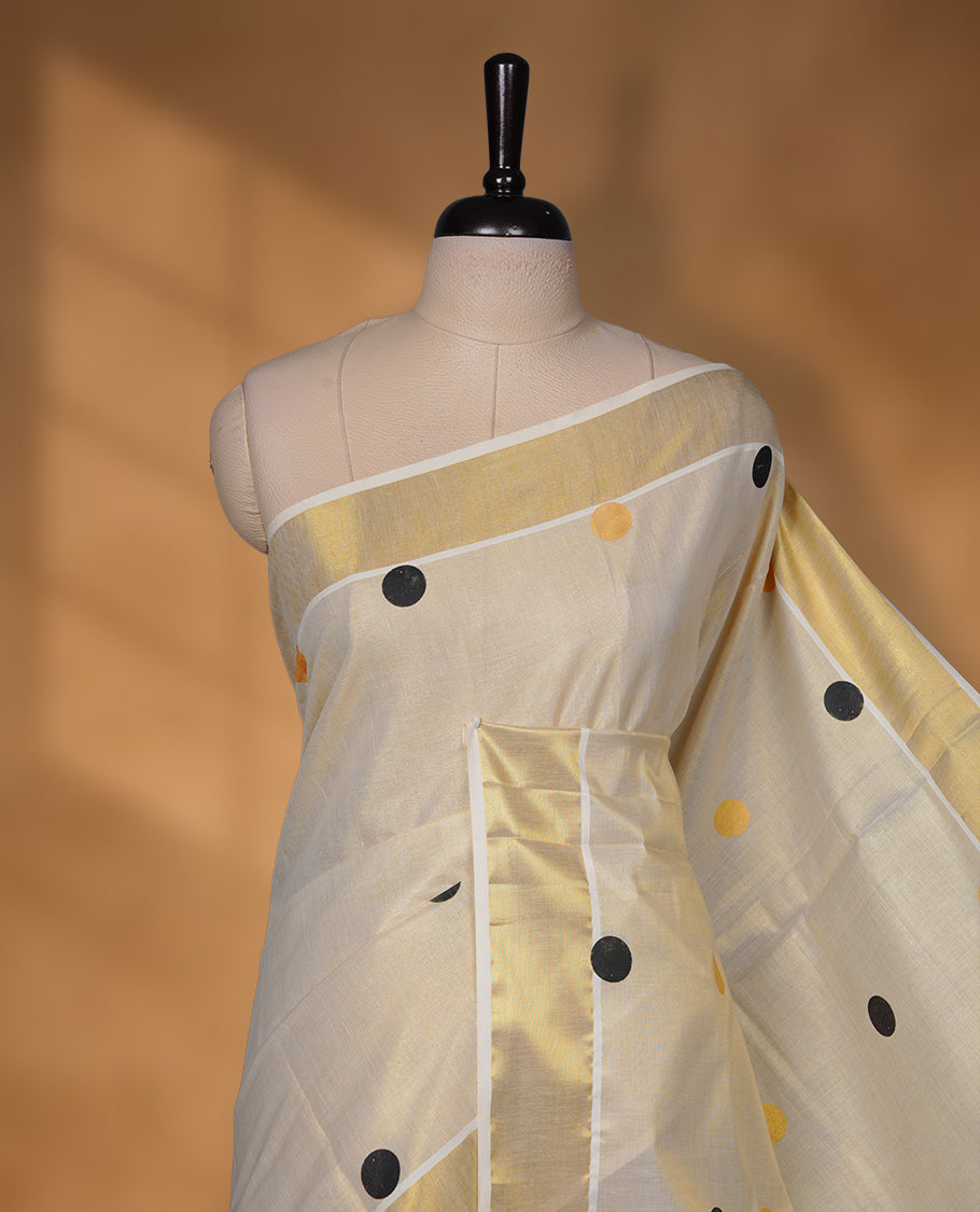 Off-white colour Tissue Kerala saree featuring playful black and gold polka buttas across the body, finished with a classic gold kasavu border and paired with a matching blouse.