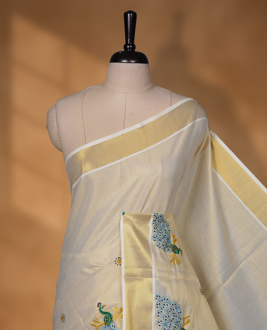Off-white Kerala saree featuring a classic gold kasavu border, highlighted with graceful blue peacock motifs across the body and pallu, and paired with a matching blouse.