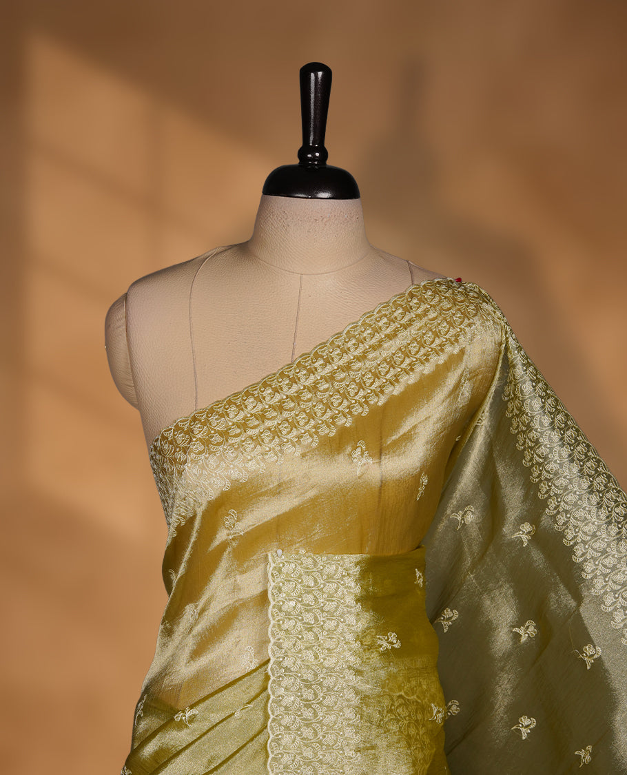 Pastel olive colour organza saree featuring white thread embroidery motifs on body and  thread detailing on the border and paired matching blouse.