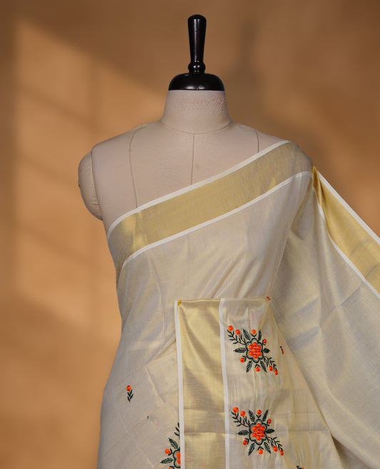 Off-white colour tissue Kerala saree with a classic gold kasavu border, highlighted by delicate orange floral embroidery across the body and pallu, and paired with a matching blouse.
