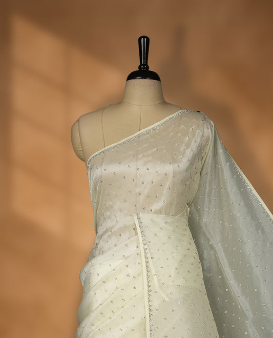 Cream Colour net shimmer fancy saree adorned with white stone buttas all over the body, paired with a delicate stone worked border and matching blouse