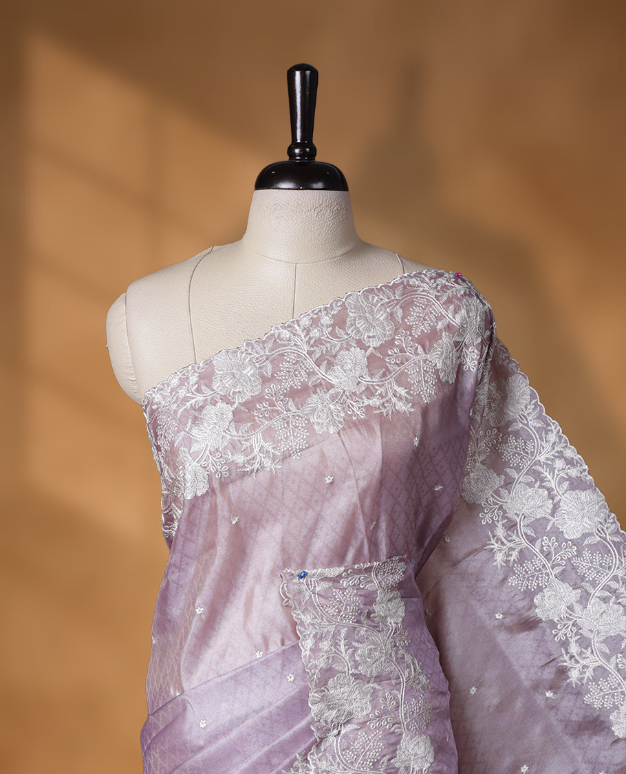 Lavender colour organza designer saree featuring a subtle self patterned body and an intricately scalloped floral thread embroidered border all around, complemented by a coordinating embroidered pallu and paired with a matching blouse.