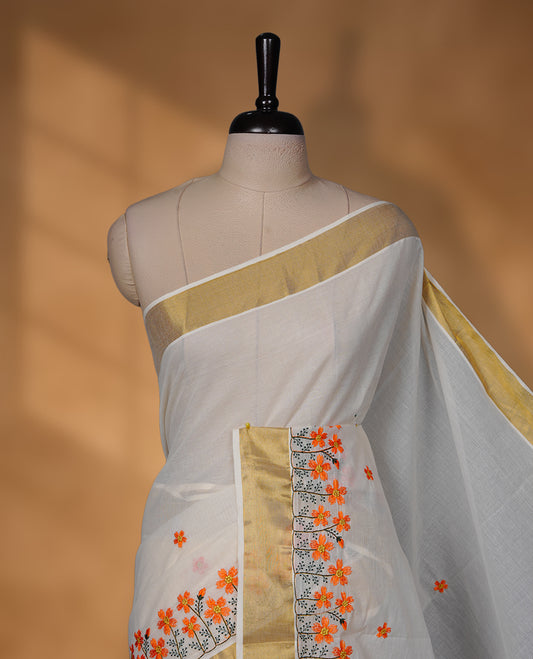 Off-white colour Kerala saree with a classic gold kasavu border, delicately embroidered floral motifs in orange and green across the body and pallu, finished with a subtle golden sheen for timeless elegance.