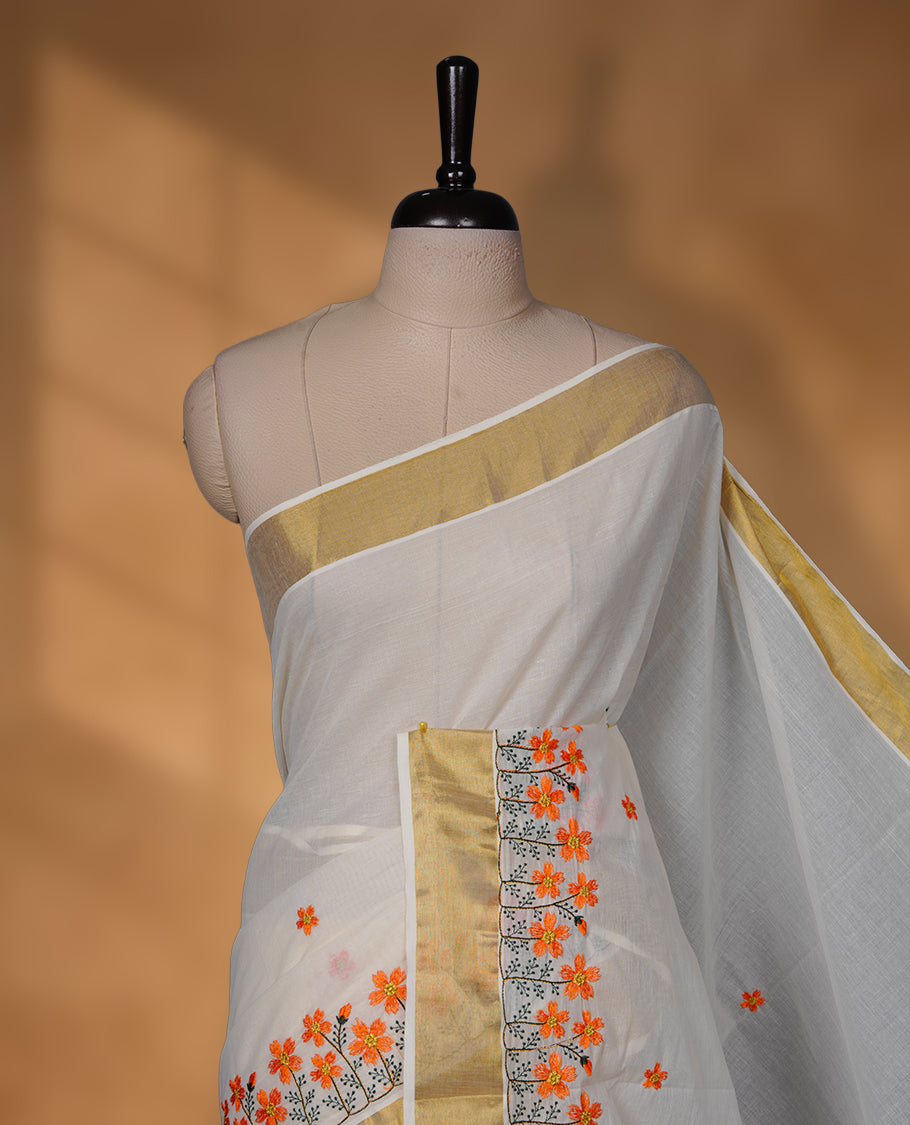 Off-white colour Kerala saree with a classic gold kasavu border, delicately embroidered floral motifs in orange and green across the body and pallu, finished with a subtle golden sheen for timeless elegance.