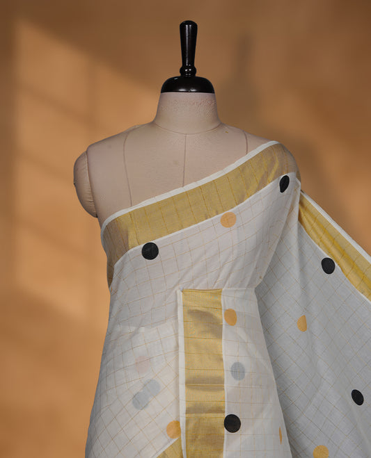 Off-white colour cotton Kerala saree with a classic gold kasavu border, highlighted by subtle gold checks and playful black & mustard polka dot motifs across the body and pallu, paired with a matching blouse.