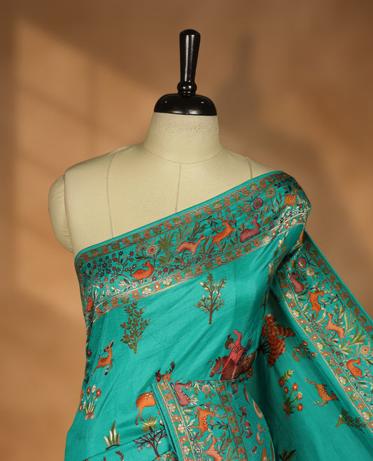 Turquoise sea green colour Pashmina silk saree lavishly adorned with all‑over woven wildlife and forest motifs, framed by an intricately detailed animal & floral zari border and grand storytelling pallu, paired with a matching woven border blouse piece.